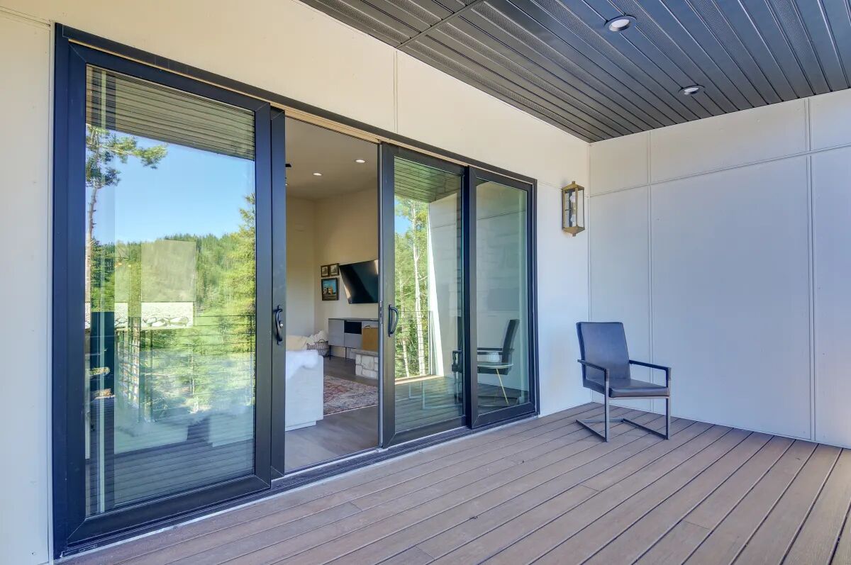 A modern outdoor area with a wooden deck, a glass door leading to an interior space, and a chair.