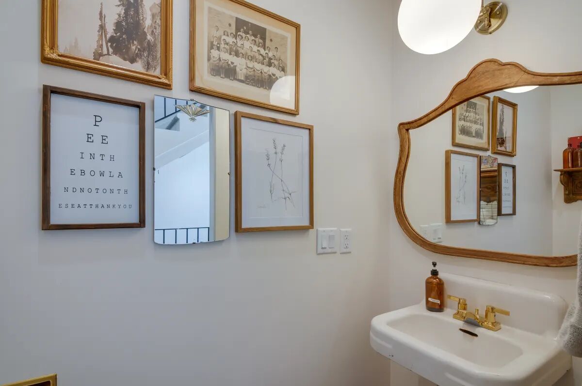 Een badkamer met een witte wastafel, een spiegel en foto's in lijsten aan de muur.