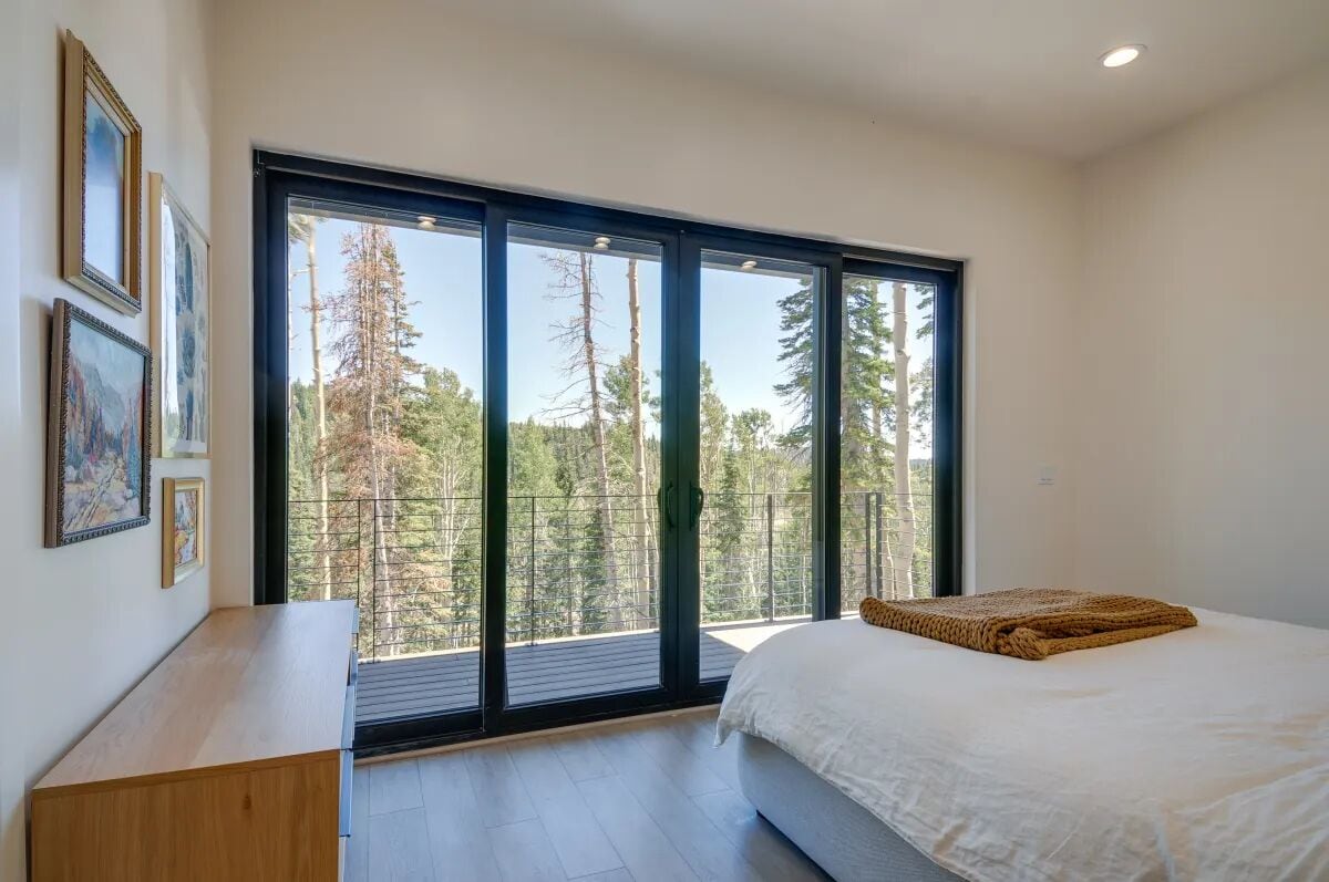 A bedroom with a large sliding glass door leading to a balcony, a bed with a white comforter, and a wooden nightstand.