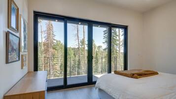 A bedroom with a large sliding glass door leading to a balcony, a bed with a white comforter, and a wooden nightstand.