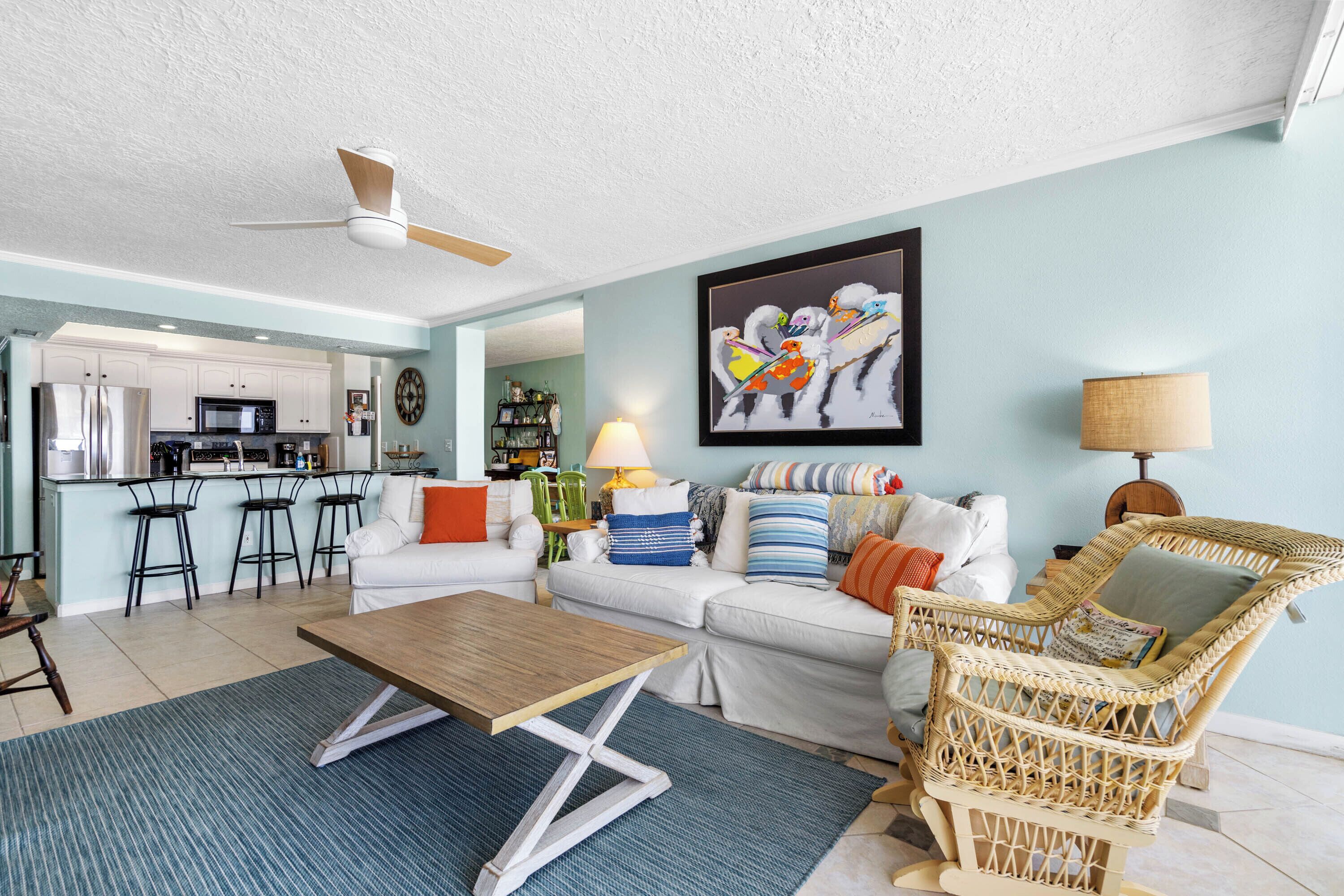 A modern living room with a wooden coffee table, a wicker chair, and a sofa with colorful cushions.