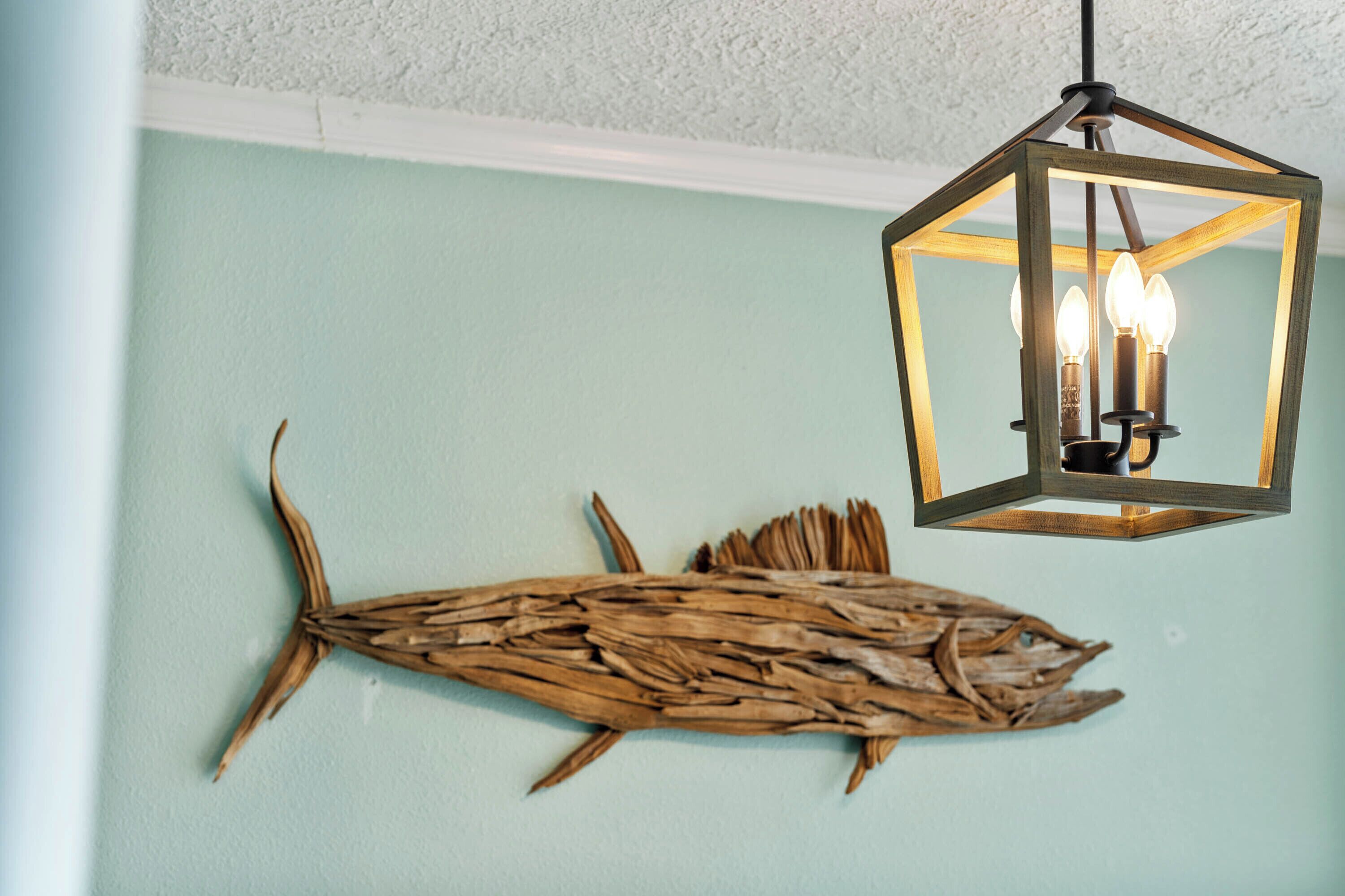 A wall with a wooden fish decoration and a hanging light fixture.