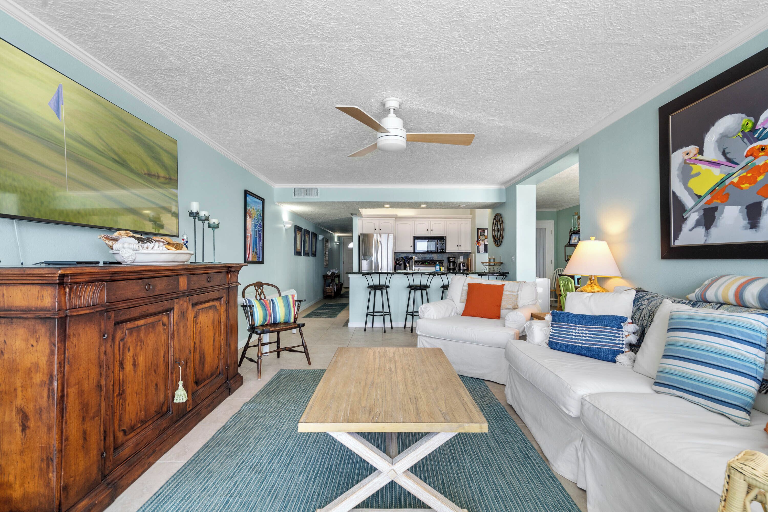 A spacious living room with a wooden coffee table, a white sofa, and a kitchen in the background.
