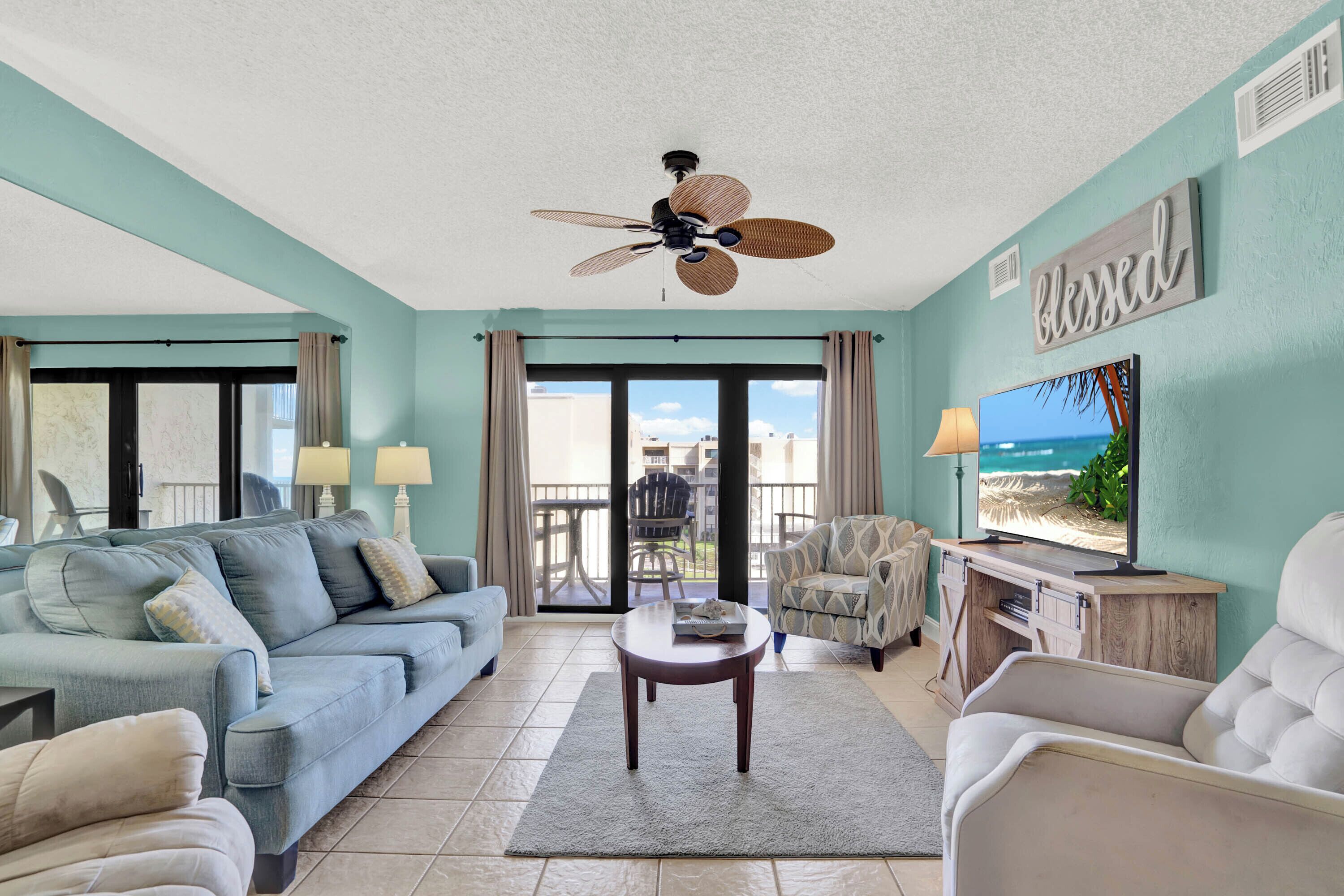 A living room with a ceiling fan, a sofa, a coffee table, a TV, and a view of the outdoors.