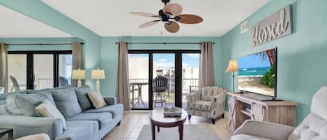 A living room with a ceiling fan, a sofa, a coffee table, a TV, and a view of the outdoors.