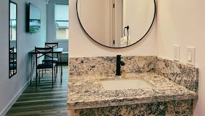 Un bagno con lavabo su piano in granito, uno specchio tondo e un corpo illuminante a parete.