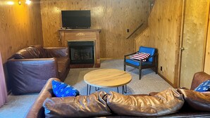 Una sala de estar acogedora con chimenea, sofás de cuero, un sillón azul y un televisor de pantalla plana sobre la chimenea.