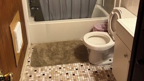 Ein Badezimmer mit Duschvorhang, Badewanne, Toilette und Fliesenboden.