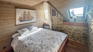 Une chambre avec un plafond en bois, un lit recouvert d’une literie à motifs floraux, une carte accrochée au mur et un mur en pierre avec une fenêtre.