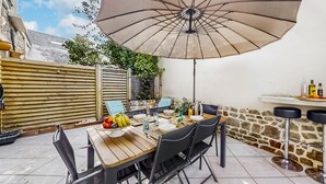 Une terrasse extérieure avec une table en bois, des chaises noires et un grand parasol.