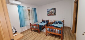A room with two wooden beds, a window with blue curtains, a wall-mounted air conditioner, and a painting. - Vivenda Do Relaxo 
 Espite district santarem  (Santarem)