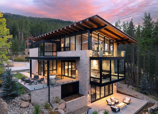 Une maison moderne à deux étages, dotée de grandes baies vitrées, d’un espace extérieur aménagé et d’une façade en pierre.