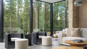 A modern living room with large windows, wicker furniture, a white sofa, and a round wooden coffee table.