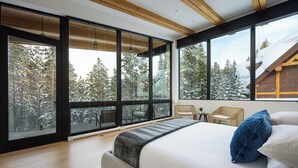 A modern bedroom with a large bed, a view of snow-covered trees, and a wooden ceiling.