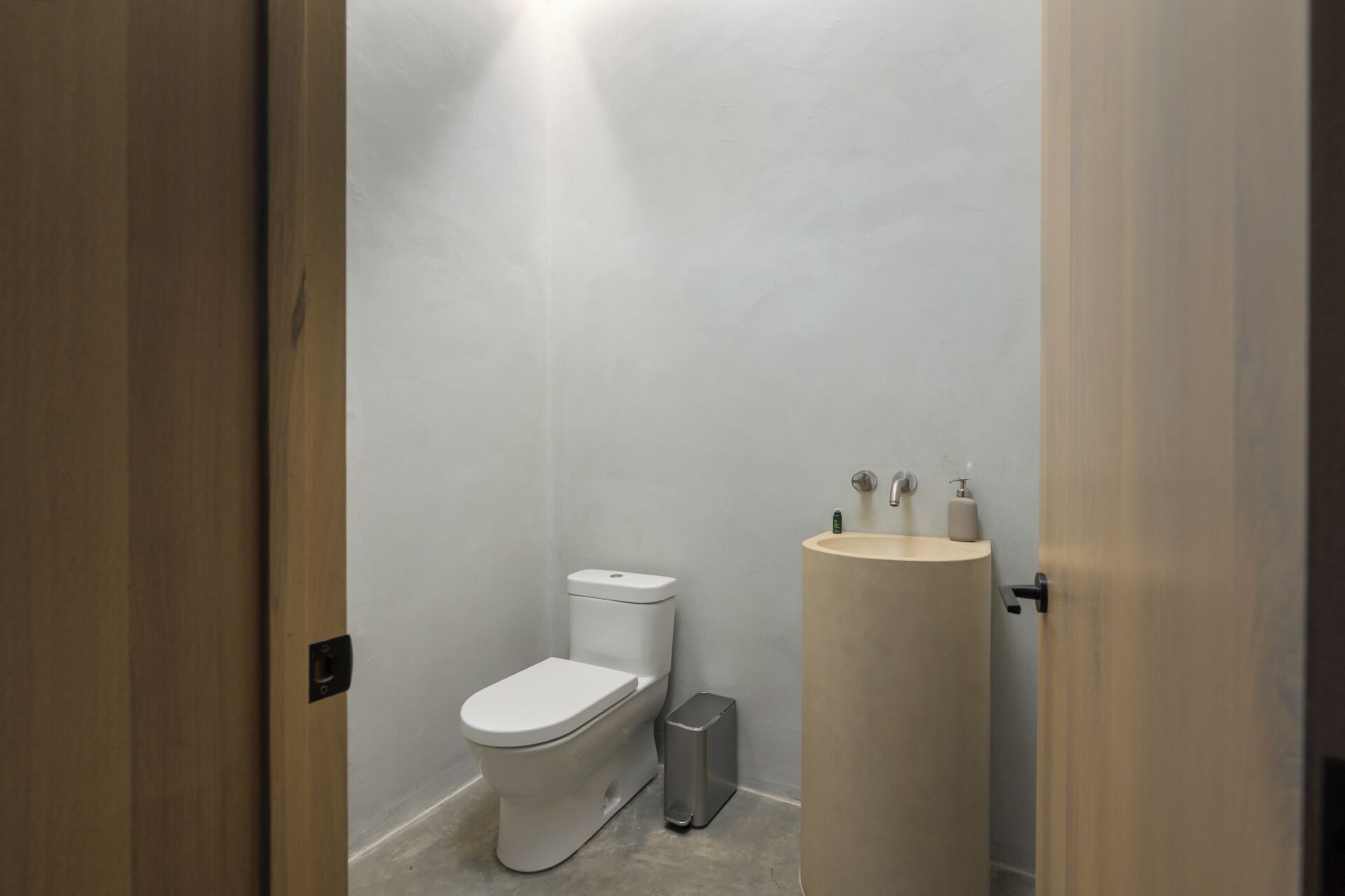 A small, modern bathroom with a toilet, a sink, and a trash bin.
