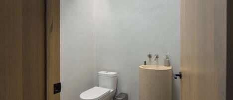 A small, modern bathroom with a toilet, a sink, and a trash bin.