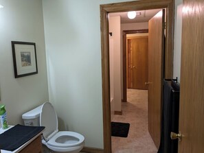 A bathroom with a toilet, a framed picture on the wall, and a door leading to another room. - Large Farmhouse in Ozark Mountains (Cape Fair)