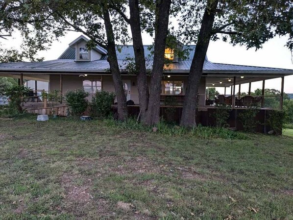 A two-story house with a covered porch and a large tree in front. - Large Farmhouse in Ozark Mountains (Cape Fair)