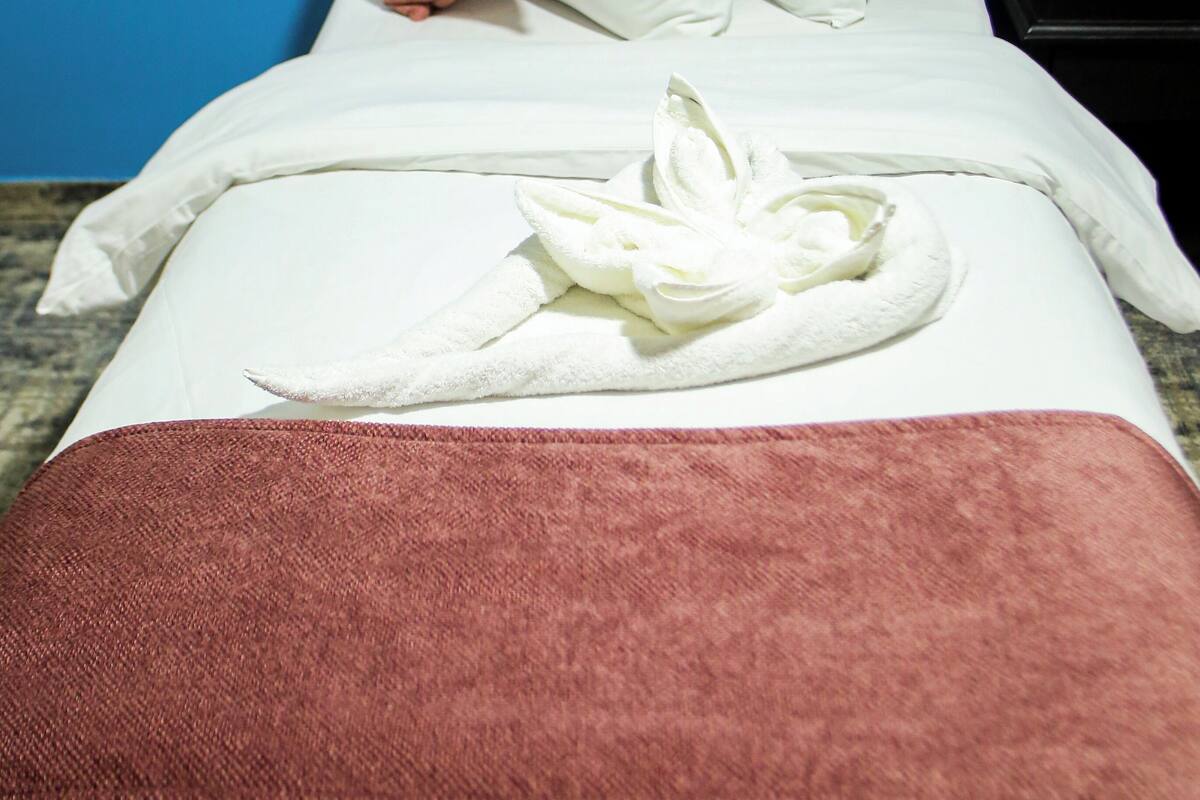 A neatly made bed with white linens, a pink pillow, and a white towel folded on the bed.