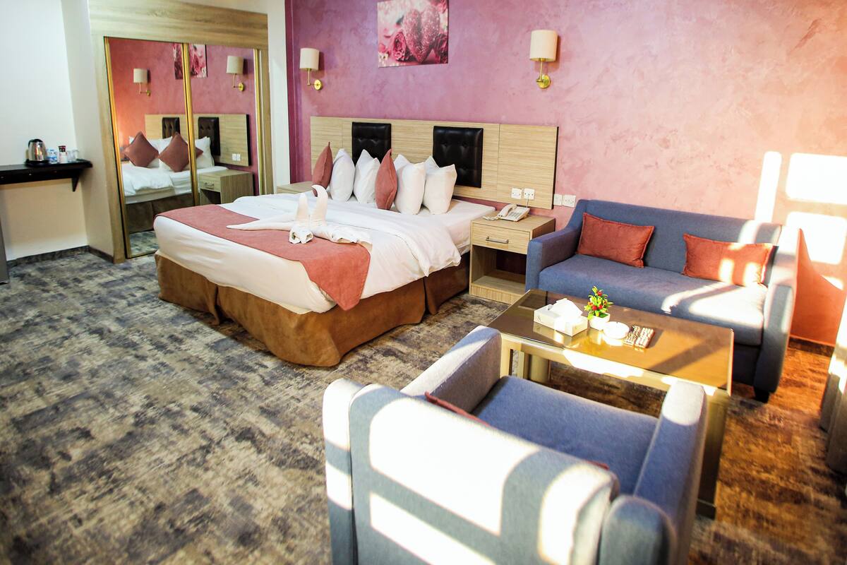 A hotel room with a large bed, a sofa, a coffee table, and a desk with a phone.