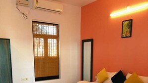 A bedroom with a bed, a chair, a window with blinds, an air conditioning unit, and a wall-mounted light fixture. - Tiger Tales Resort (Palia Kalan)