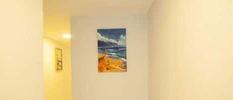 A narrow hallway with a painting of a beach scene on the wall.
