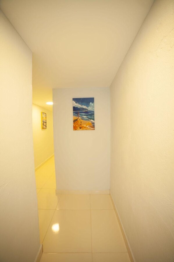 A narrow hallway with a painting of a beach scene on the wall. - JM GUESTHOUSE (Santo Domingo)