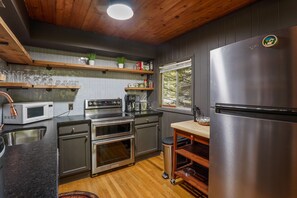 Eine moderne Küche mit Edelstahlgeräten, Holzschränken und einem Fenster mit Blick ins Freie.
