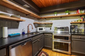 A modern kitchen with stainless steel appliances, wooden shelves, and a tiled backsplash. - Chicory Cliffs | Hocking Hills, Views, Hot Tub (Rockbridge)