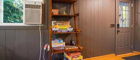 A wooden bookshelf filled with board games, an air conditioning unit, and a door with a window.