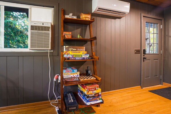 A wooden bookshelf filled with board games, an air conditioning unit, and a door with a window.