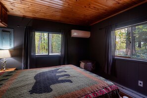 Ein Schlafzimmer mit einem großen Bett, zwei mit Vorhängen versehenen Fenstern, einer Klimaanlage und einer Holzbalkendecke.