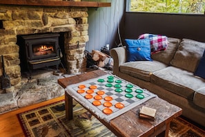 A stone fireplace with a fire, a checkered board game, and a sofa with a blanket and pillows.