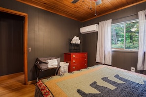 A bedroom with dark wooden walls, a red dresser, a quilted bedspread, and a window with a view of trees. - Chicory Cliffs | Hocking Hills, Views, Hot Tub (Rockbridge)