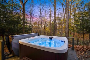 A hot tub on a wooden deck with a forest view.