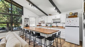 Una cocina moderna con una isla central, armarios blancos y un amplio ventanal con vistas a un jardín.