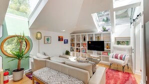 A modern living room with a sofa, armchair, and a TV. There are bookshelves, a plant, and a fire extinguisher. - Pet-Friendly Minneapolis Studio: Walk to Lake! (Minneapolis)