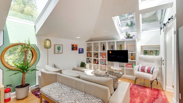 A modern living room with a sofa, armchair, and a TV. There are bookshelves, a plant, and a fire extinguisher. - Pet-Friendly Minneapolis Studio: Walk to Lake! (Minneapolis)