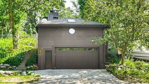 A two-story house with a garage, surrounded by lush greenery and a stone staircase leading to the entrance. - Pet-Friendly Minneapolis Studio: Walk to Lake! (Minneapolis)