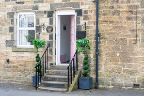 A stone building with a pink door, a staircase with black railings, and potted plants. - Northern Hideaways, Castle View (Bellingham)
