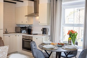 A modern kitchen with white cabinetry, a dining table set with plates, glasses, and a vase of flowers. - Northern Hideaways, Castle View (Bellingham)