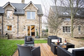 A stone house with a wooden deck, outdoor seating, and a stone wall.