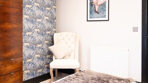 A room with a patterned wallpaper, a framed artwork on the wall, a tufted chair, and a radiator. - Northern Hideaways, Apple Store, Ellingham (Chathill)