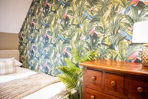 Ein Schlafzimmer mit einem Bett, einer Holzkommode und tropisch gestalteter Tapete.