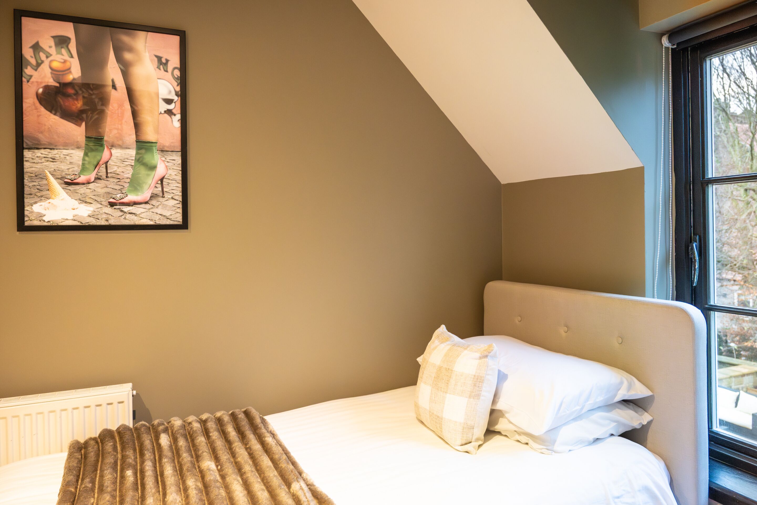 A bedroom with a bed, a window, and a wall-mounted picture.