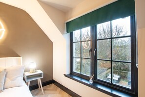 A bedroom with a bed, bedside table, and a window with a view of the outdoors.