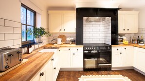 A modern kitchen with white cabinets, a black stove, and a wooden countertop. - Northern Hideaways, Apple Store, Ellingham (Chathill)