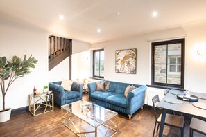 Ein modernes Wohnzimmer mit einem blauen Sofa, einem Glastisch und einem Essbereich mit Tisch und Stühlen.