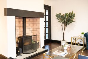 A modern living room with a fireplace, a glass coffee table, a potted plant, and a blue sofa.