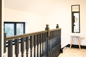 A staircase with a black railing and a white wall with a mirror and a small white shelf.